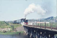 Locomotive with passengers approaching bridge from the town