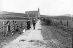 A couple with a dog walking the road from the Borth church to the station