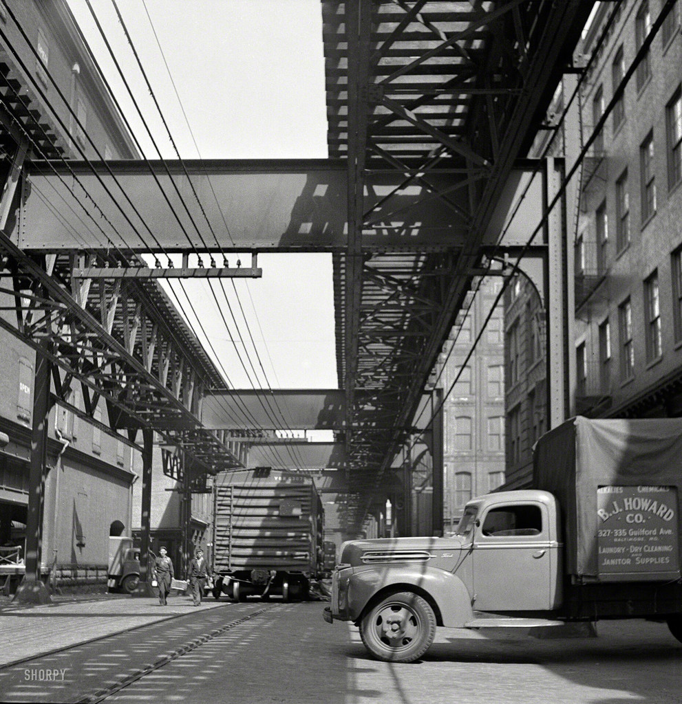 Trucks and trains unloading goods underneath elevated trolley
