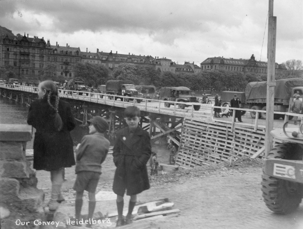 German children look on as an American Army convoy crosses a newly constructed bridge in Germany