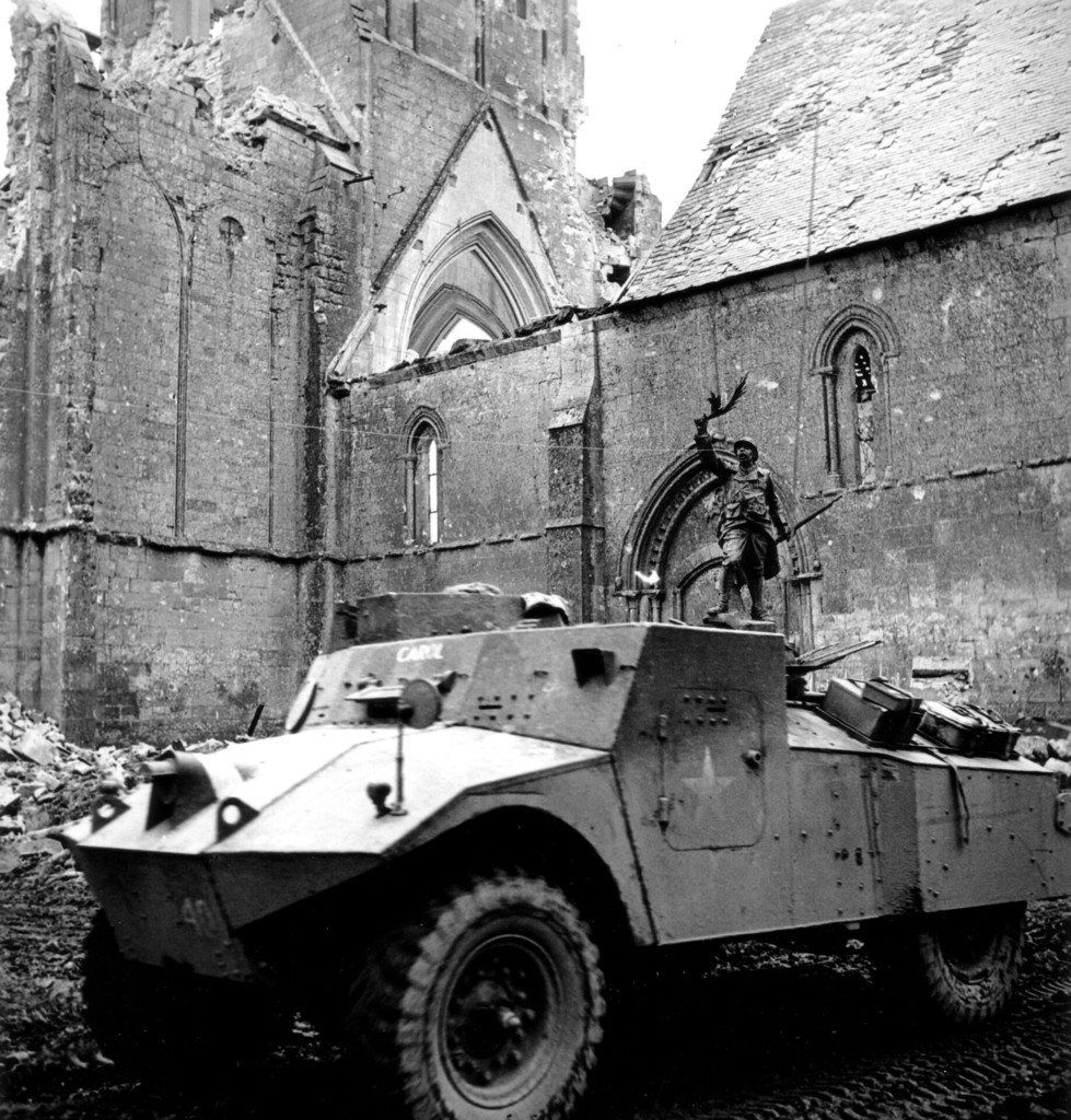 Une auto-mitrailleuse Morris devant l'église de Norrey-en-Bessin et son monument aux Morts