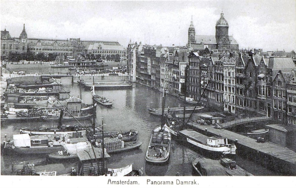 Damrak met diverse schepen en op de achtergrond het Centraal Station en de Sint Nicolaaskerk