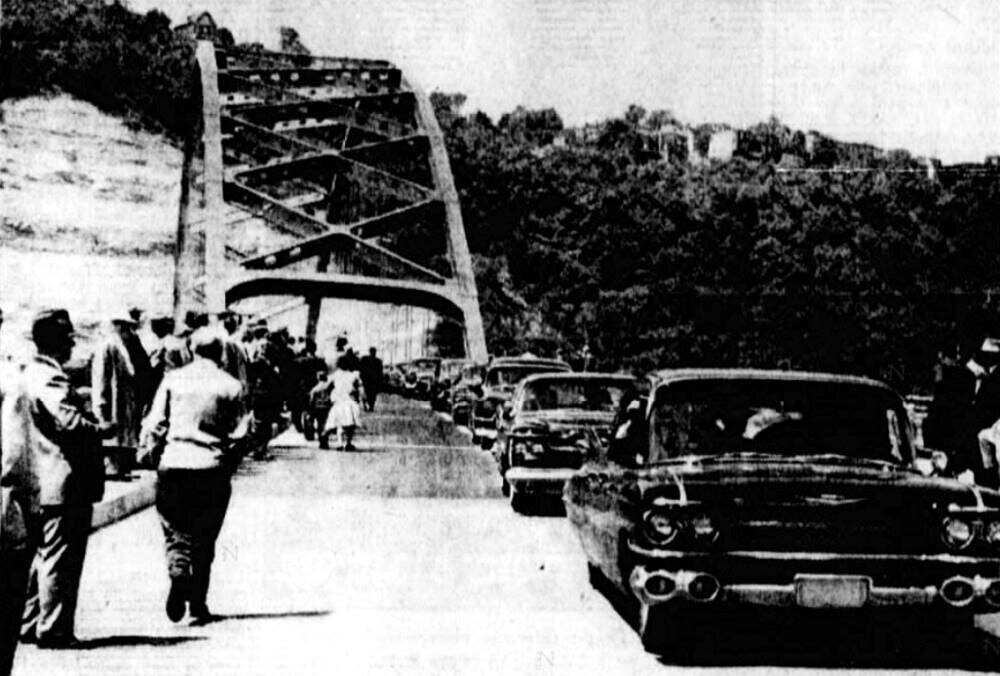 People walk onto the new bridge while the procession of vehicles passes over on dedication day