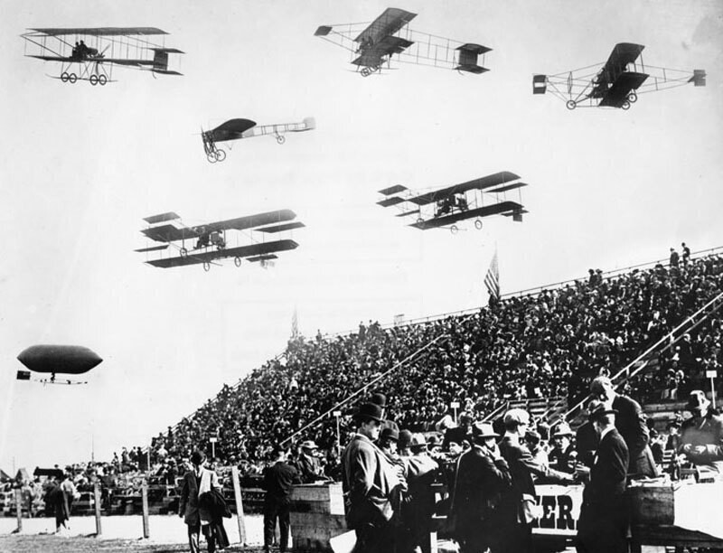 6 biplanes and 1 airship over crowd
